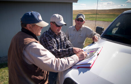 Three men looking at a map in a grasslands